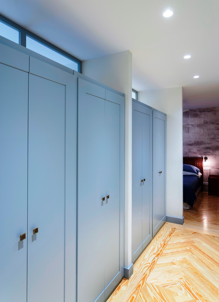 Foto de armario unisex actual grande con armarios con paneles empotrados, puertas de armario azules y suelo de madera clara