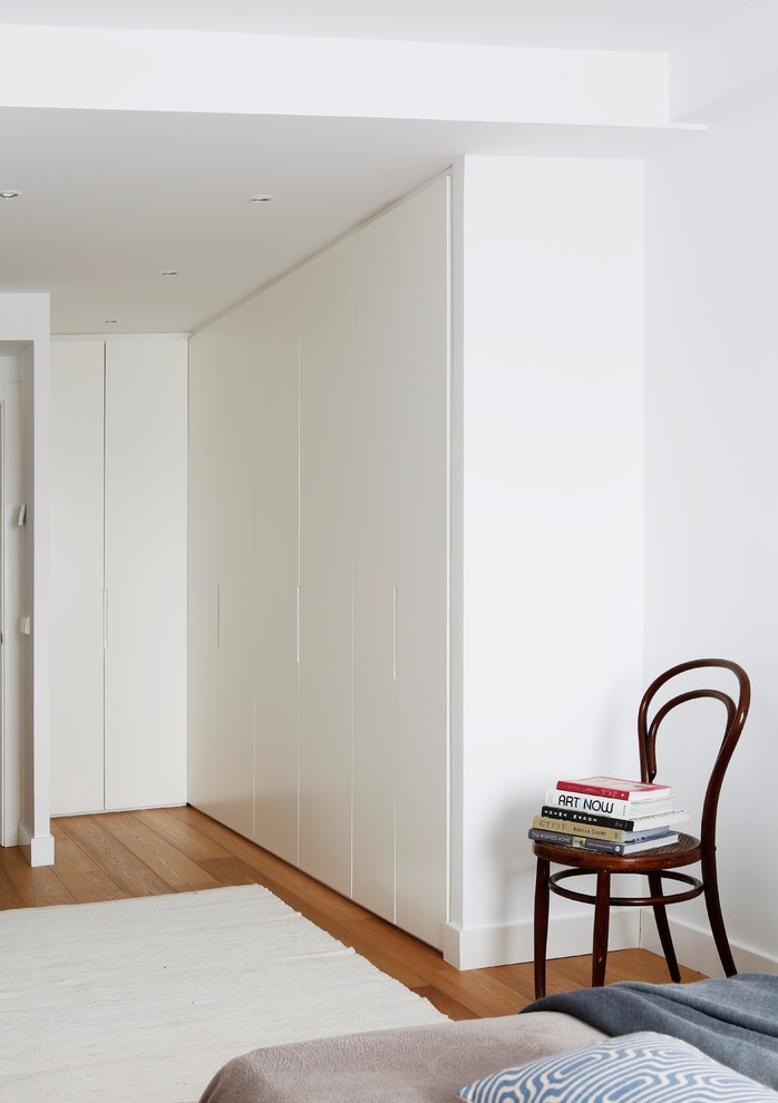 Diseño de armario unisex escandinavo de tamaño medio con armarios con paneles lisos, puertas de armario blancas y suelo de madera en tonos medios