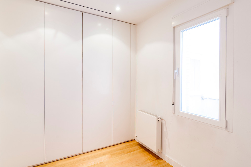 Diseño de armario unisex contemporáneo de tamaño medio con armarios con paneles lisos, puertas de armario blancas y suelo de madera en tonos medios