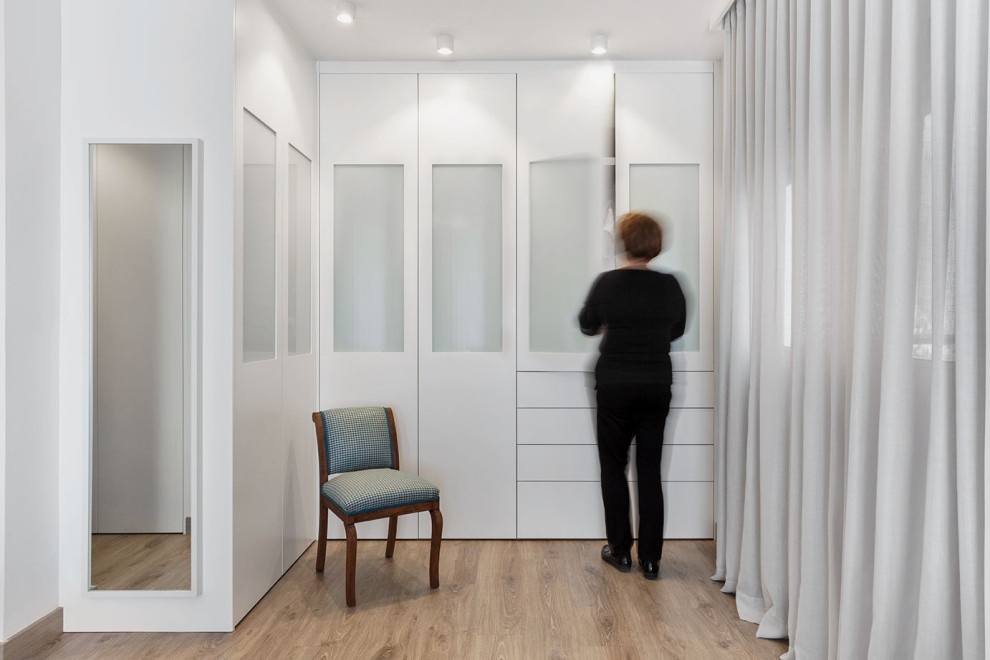 Immagine di una cabina armadio per donna minimalista di medie dimensioni con ante di vetro, ante bianche, pavimento in laminato e pavimento beige