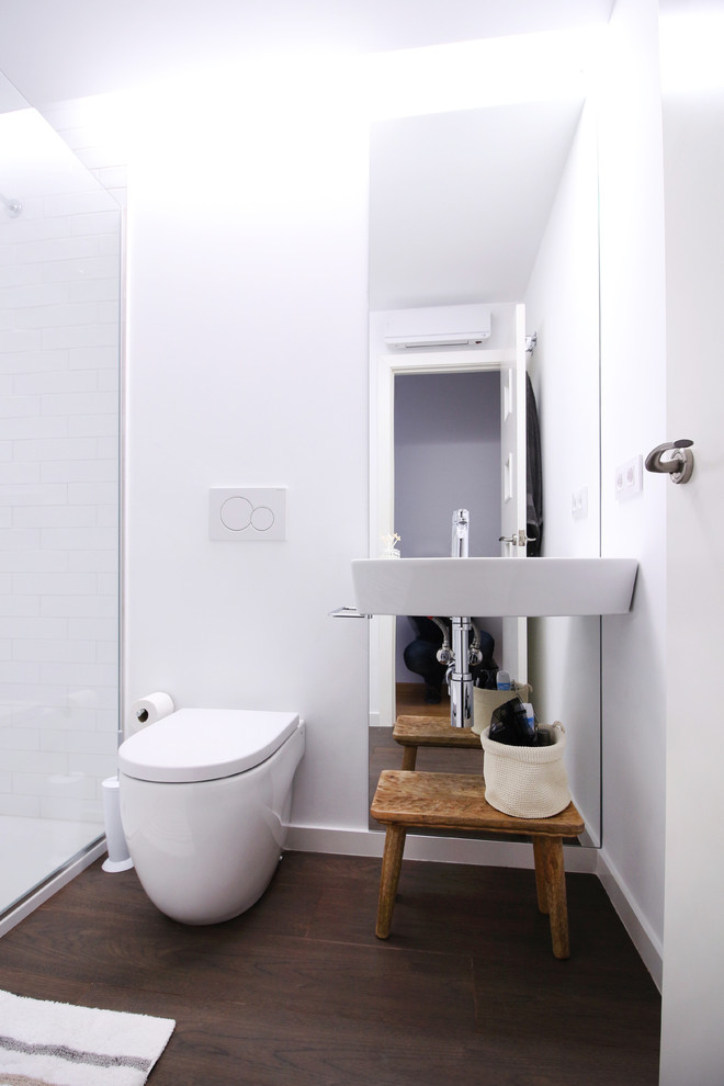 На фото: туалет среднего размера в современном стиле с унитазом-моноблоком, белыми стенами, темным паркетным полом и подвесной раковиной