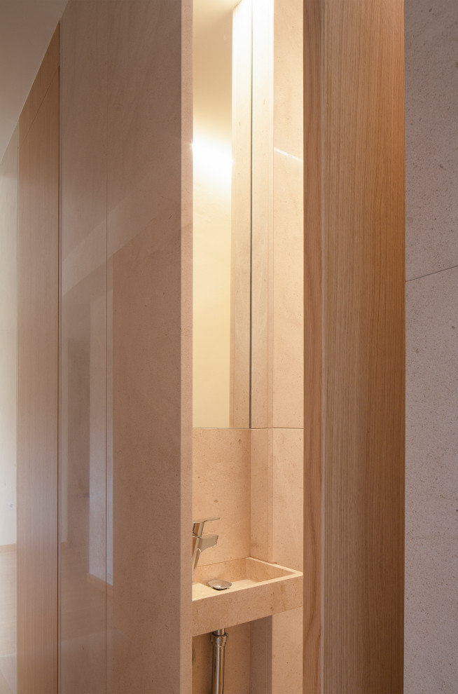 This is an example of a small contemporary cloakroom in Valencia with flat-panel cabinets, medium wood cabinets, a wall mounted toilet, beige tiles, limestone tiles, beige walls, limestone flooring, a submerged sink, limestone worktops, beige floors and beige worktops.