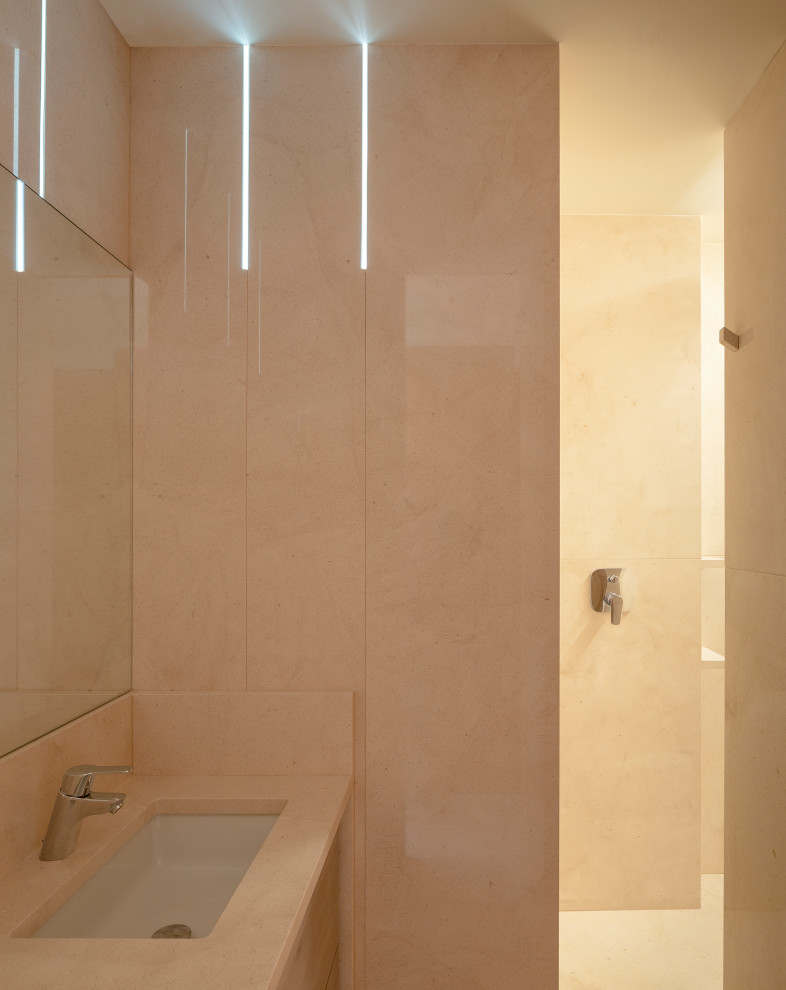 Cette image montre un petit WC suspendu design en bois brun avec un placard à porte plane, un carrelage beige, du carrelage en pierre calcaire, un mur beige, un sol en calcaire, un lavabo encastré, un plan de toilette en calcaire, un sol beige et un plan de toilette beige.