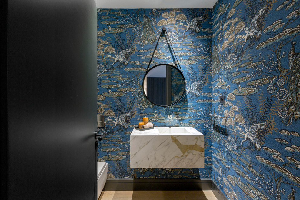 Moderne Gästetoilette mit blauer Wandfarbe, braunem Holzboden, braunem Boden, weißer Waschtischplatte, schwebendem Waschtisch und Tapetenwänden in Sonstige