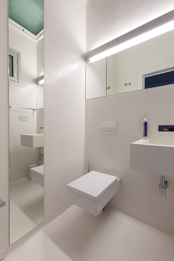 Immagine di un piccolo bagno di servizio minimal con WC sospeso, piastrelle bianche, pareti bianche, pavimento in cemento, lavabo sospeso, top in cemento, pavimento bianco e top bianco