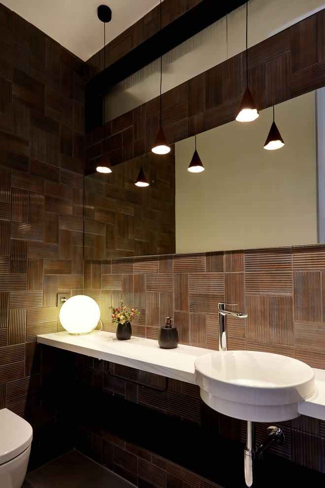 На фото: туалет среднего размера в стиле модернизм с открытыми фасадами, унитазом-моноблоком, коричневой плиткой, коричневыми стенами, бетонным полом, накладной раковиной, серым полом и белой столешницей