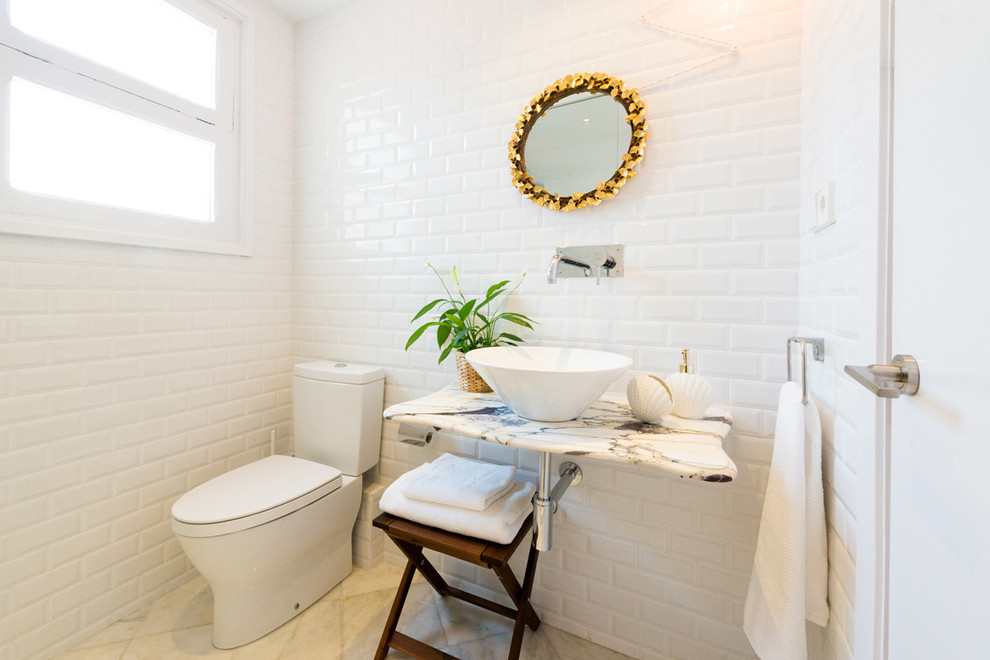 Photo of a small scandi cloakroom in Barcelona with a two-piece toilet, metro tiles, white walls, travertine flooring, a vessel sink, marble worktops and white tiles.
