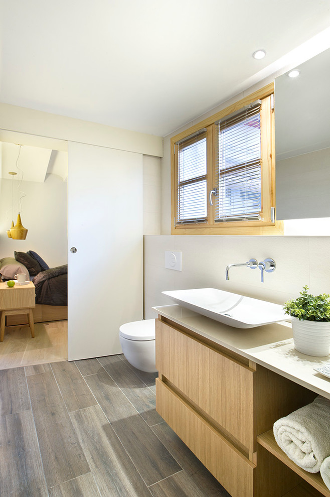 Mittelgroße Moderne Gästetoilette mit hellbraunen Holzschränken, Wandtoilette, weißer Wandfarbe, Aufsatzwaschbecken und flächenbündigen Schrankfronten in Madrid