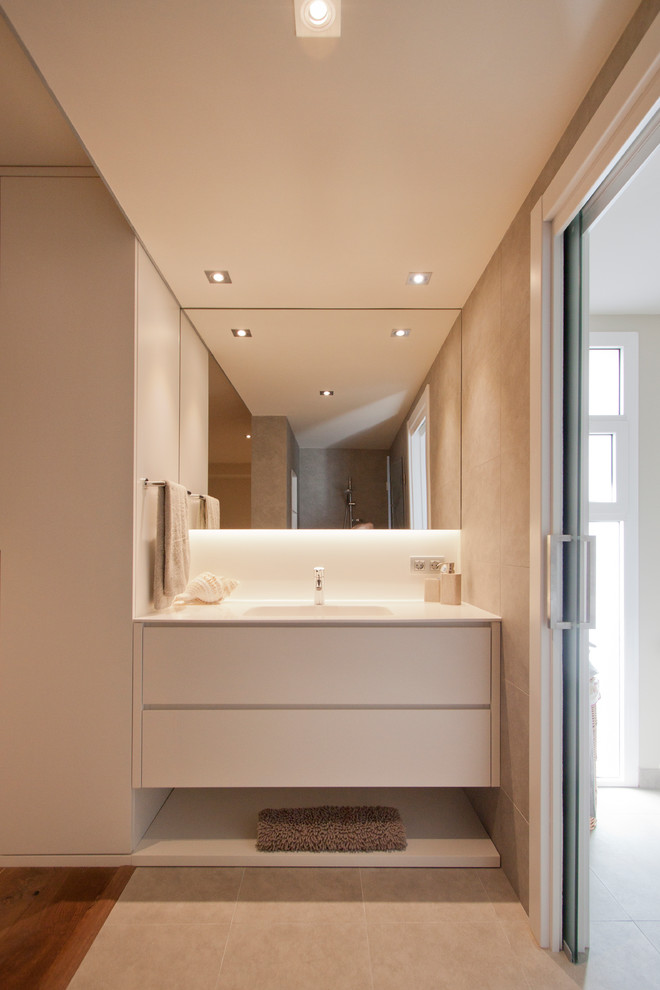 Cette image montre un WC et toilettes design de taille moyenne avec un mur beige, un lavabo intégré, un placard à porte plane, des portes de placard blanches et un sol en carrelage de céramique.