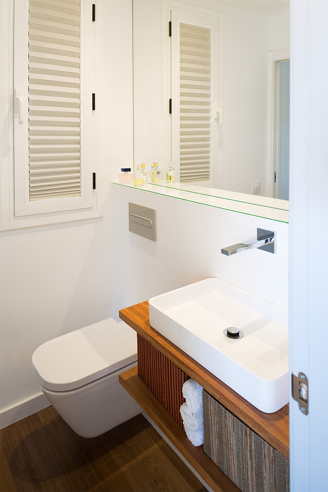 Aménagement d'un petit WC suspendu contemporain en bois brun avec un placard sans porte, un carrelage blanc, des carreaux de béton, un mur blanc, un sol en bois brun, une vasque, un plan de toilette en bois et un sol marron.