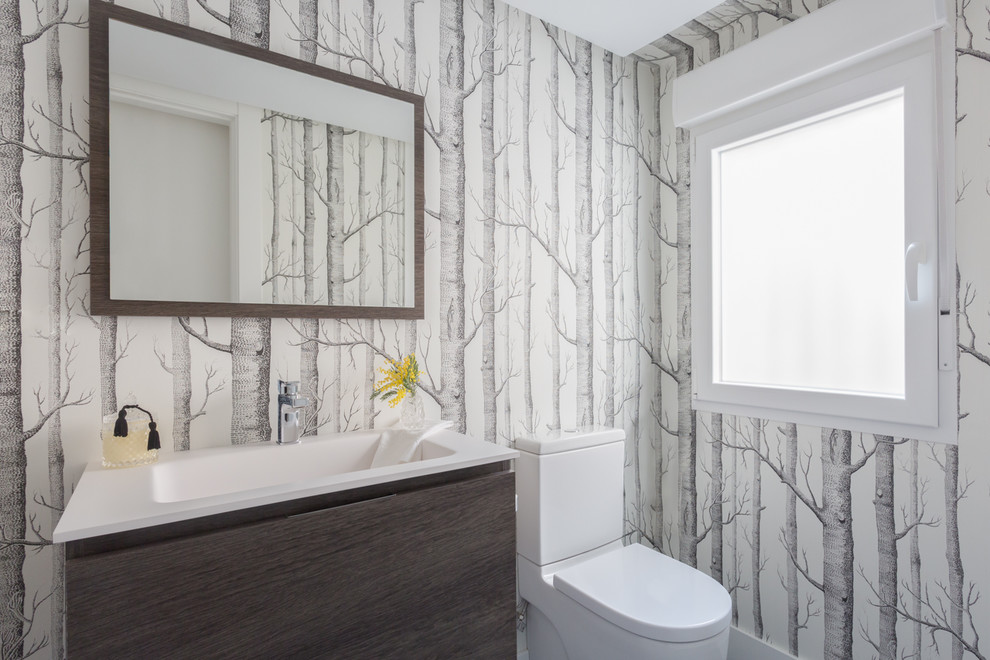 Ispirazione per un bagno di servizio design con ante lisce, ante in legno bruno, WC a due pezzi, lavabo integrato, top bianco e pareti multicolore