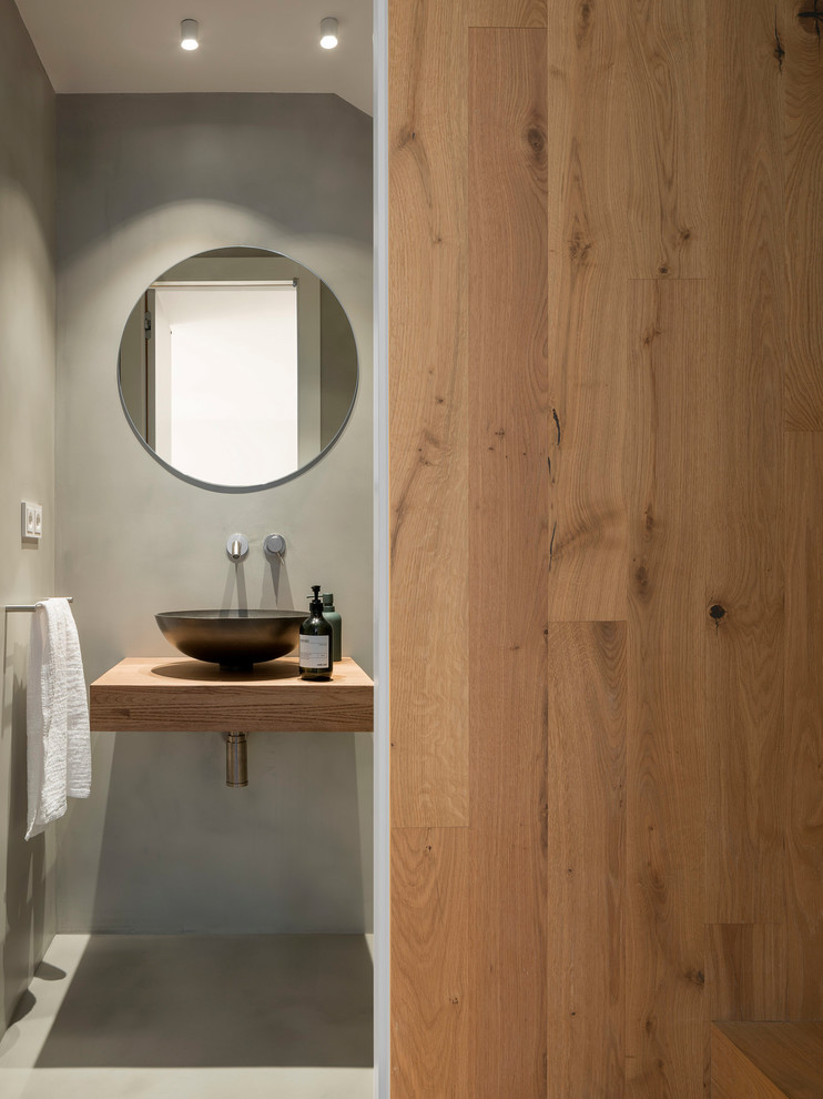 Inredning av ett nordiskt mellanstort toalett, med släta luckor, skåp i mellenmörkt trä, grå väggar, betonggolv, ett fristående handfat och grått golv