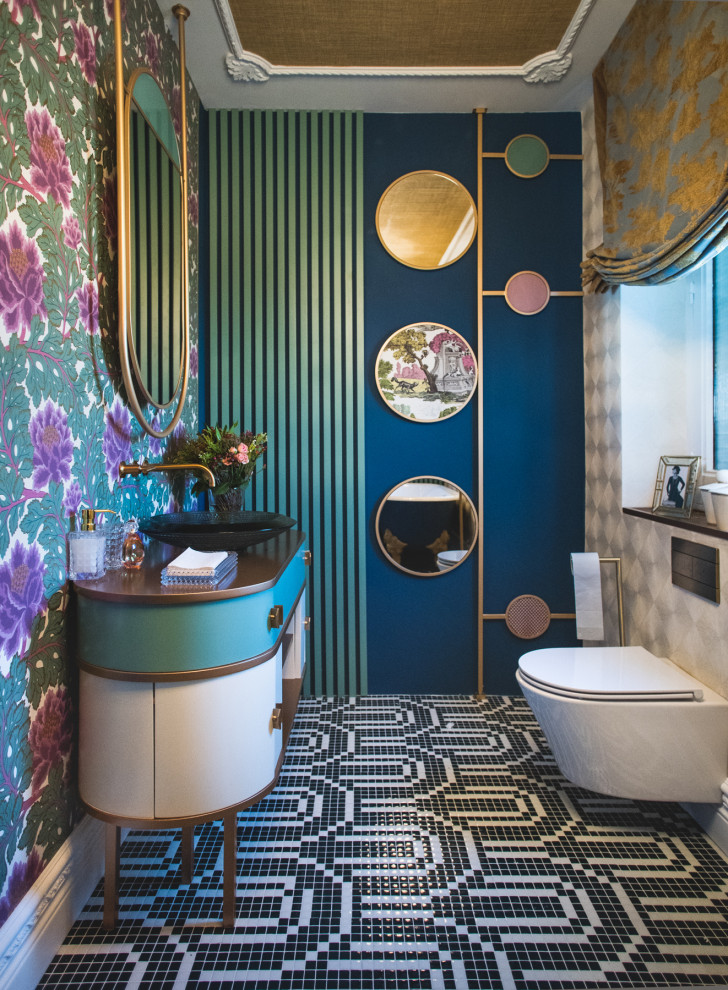 Foto på ett stort funkis brun toalett, med möbel-liknande, vita skåp, en vägghängd toalettstol, blå väggar, ett fristående handfat och flerfärgat golv