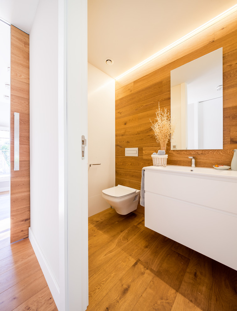 Exempel på ett mellanstort modernt toalett, med släta luckor, vita skåp, en vägghängd toalettstol, bruna väggar, mellanmörkt trägolv och ett integrerad handfat