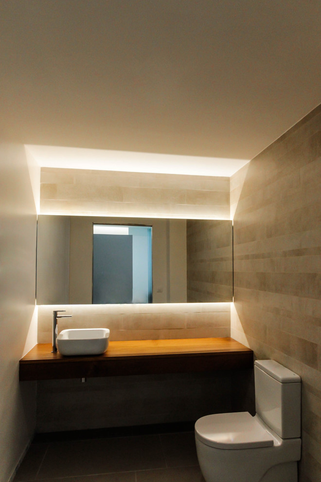 Cette image montre un WC et toilettes design de taille moyenne avec WC séparés, un mur beige, une vasque et un plan de toilette en bois.