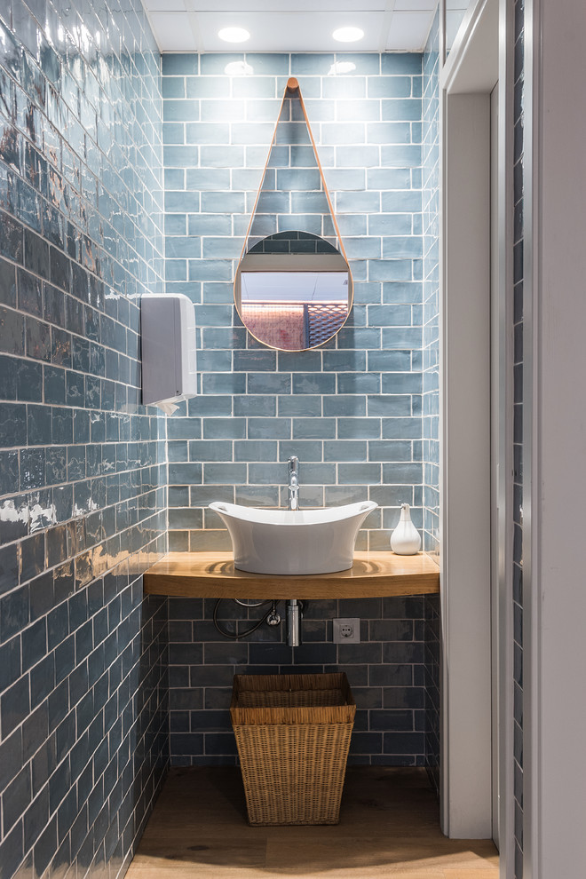 Bild på ett litet nordiskt brun brunt toalett, med blå väggar, mellanmörkt trägolv, ett fristående handfat, träbänkskiva, blå kakel och keramikplattor