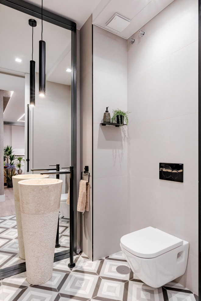 Modern inredning av ett toalett, med en vägghängd toalettstol, grå kakel, ett piedestal handfat och flerfärgat golv