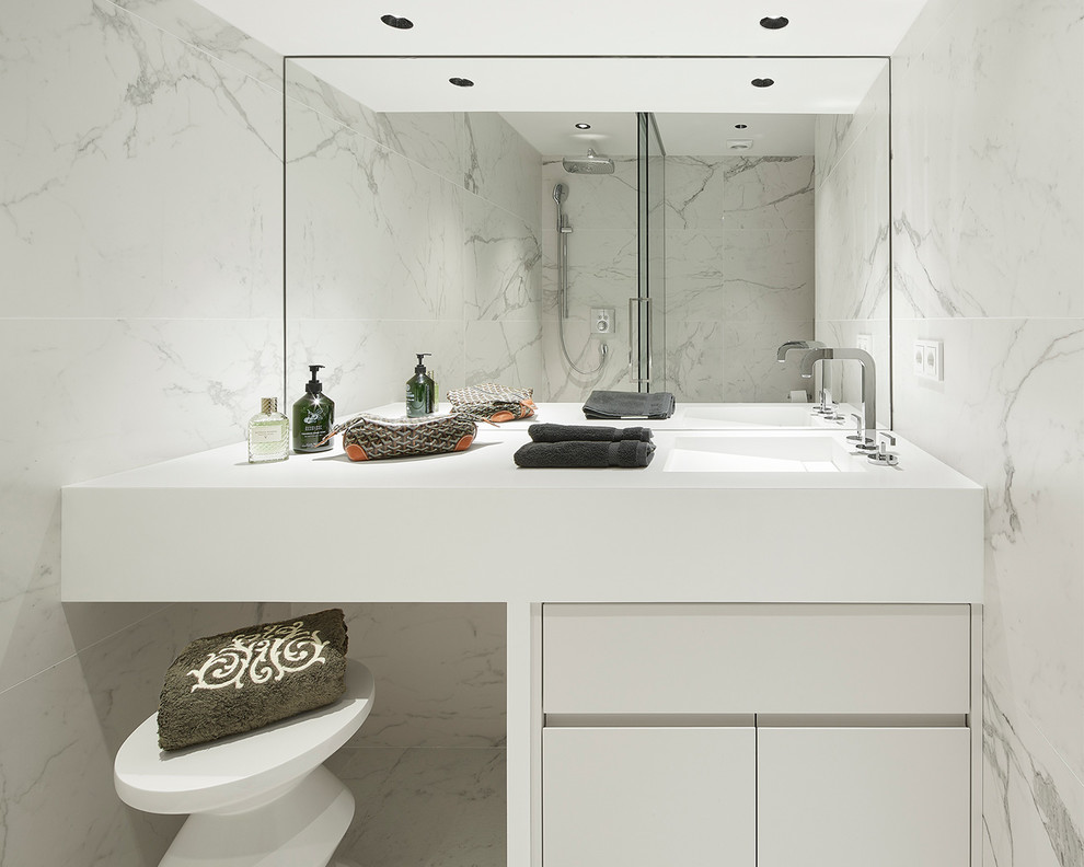 バルセロナにあるコンテンポラリースタイルのおしゃれなトイレ・洗面所 (フラットパネル扉のキャビネット、白いキャビネット、白いタイル、白い壁、一体型シンク、白い洗面カウンター、大理石タイル、大理石の床、白い床) の写真