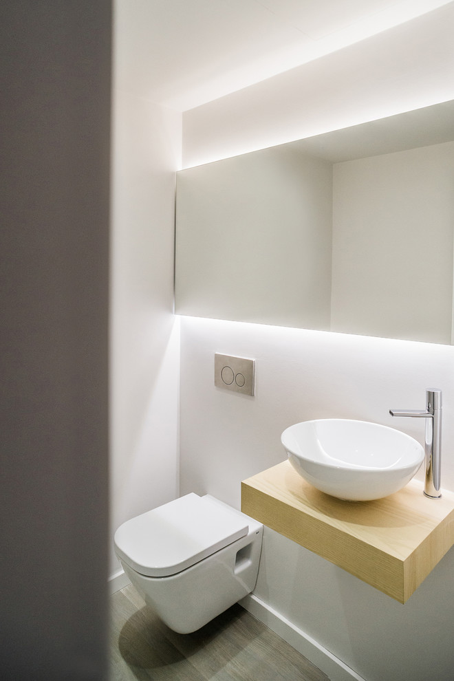 Ejemplo de aseo escandinavo pequeño con sanitario de pared, paredes blancas, lavabo sobreencimera, encimera de madera y encimeras beige