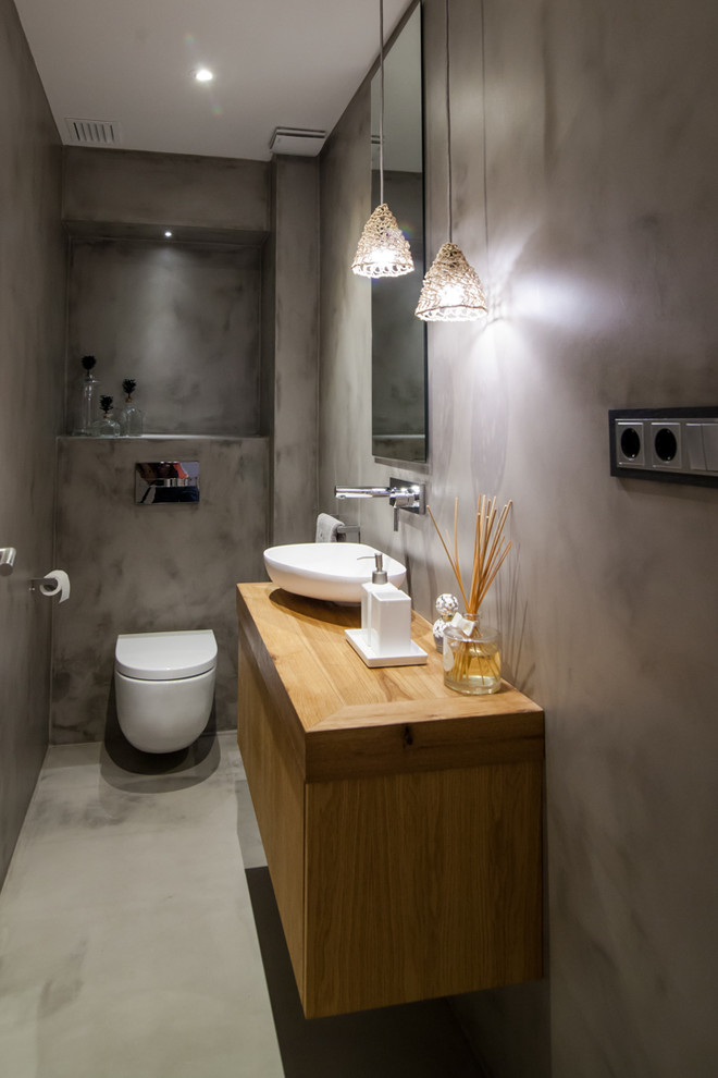 Idee per un bagno di servizio minimal di medie dimensioni con ante lisce, ante in legno scuro, WC sospeso, pareti grigie, pavimento in cemento e lavabo a bacinella