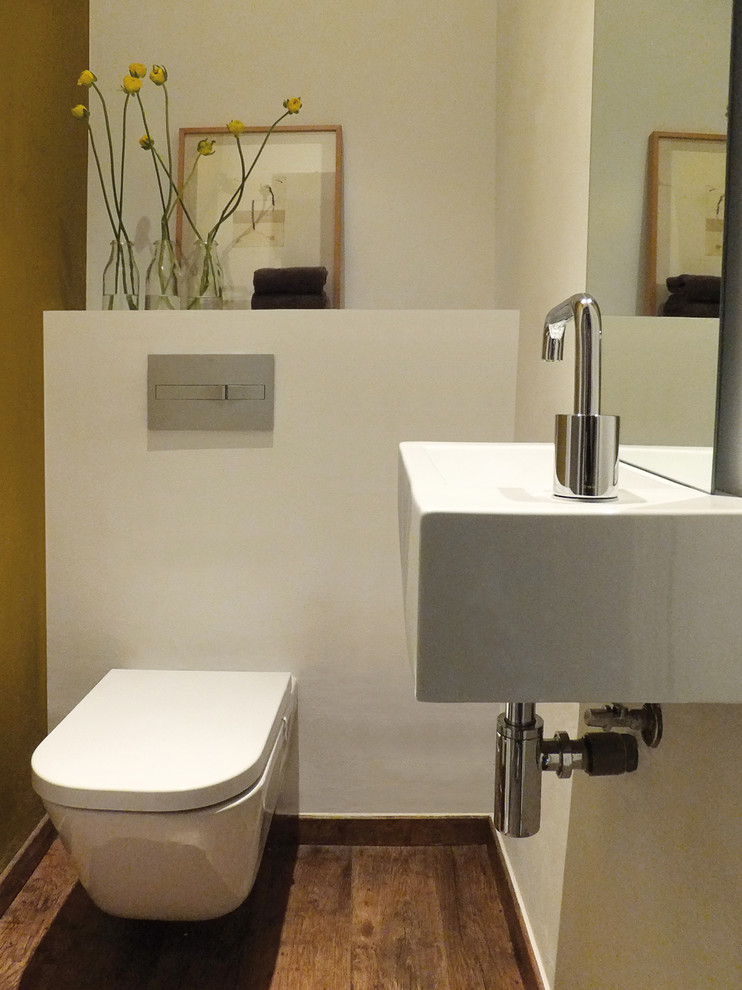 Inspiration för små moderna toaletter, med en vägghängd toalettstol, vita väggar, mellanmörkt trägolv och ett väggmonterat handfat