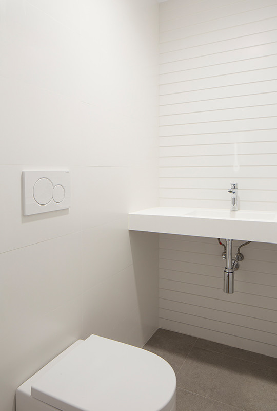 Cette photo montre un petit WC suspendu moderne avec un carrelage gris, des carreaux de céramique, un mur blanc, un sol en carrelage de céramique, un lavabo suspendu, un plan de toilette en surface solide, un sol gris et un plan de toilette blanc.