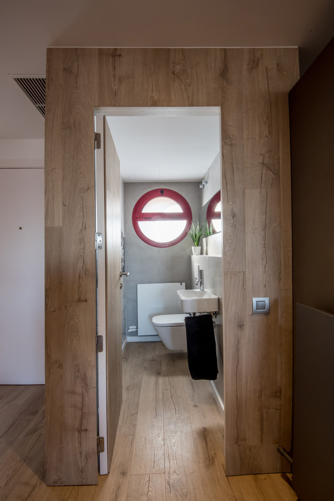 Kleine Moderne Gästetoilette mit Wandtoilette, grauen Fliesen, Zementfliesen, grauer Wandfarbe, Laminat, Wandwaschbecken und braunem Boden in Barcelona