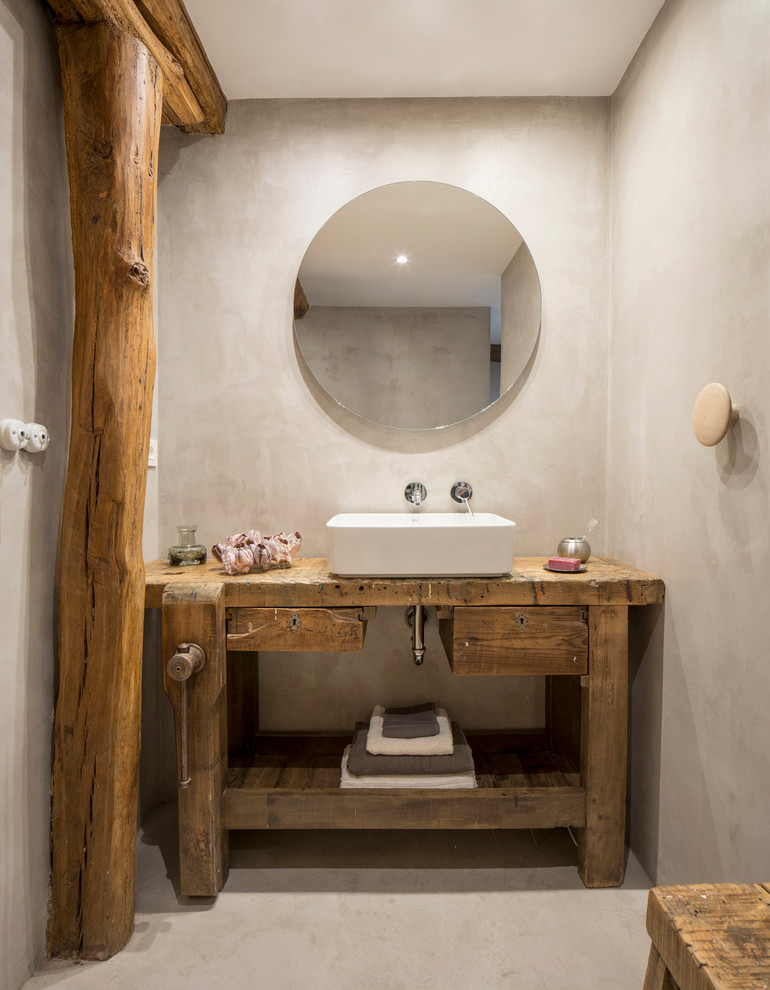Rustik inredning av ett toalett, med möbel-liknande, skåp i mellenmörkt trä, grå väggar, betonggolv, ett fristående handfat, träbänkskiva och grått golv
