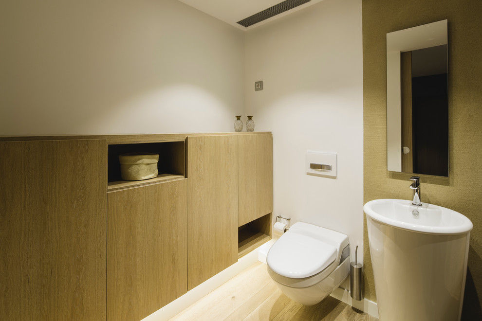 Ejemplo de aseo clásico renovado de tamaño medio con sanitario de pared, paredes blancas, suelo de madera clara y lavabo con pedestal