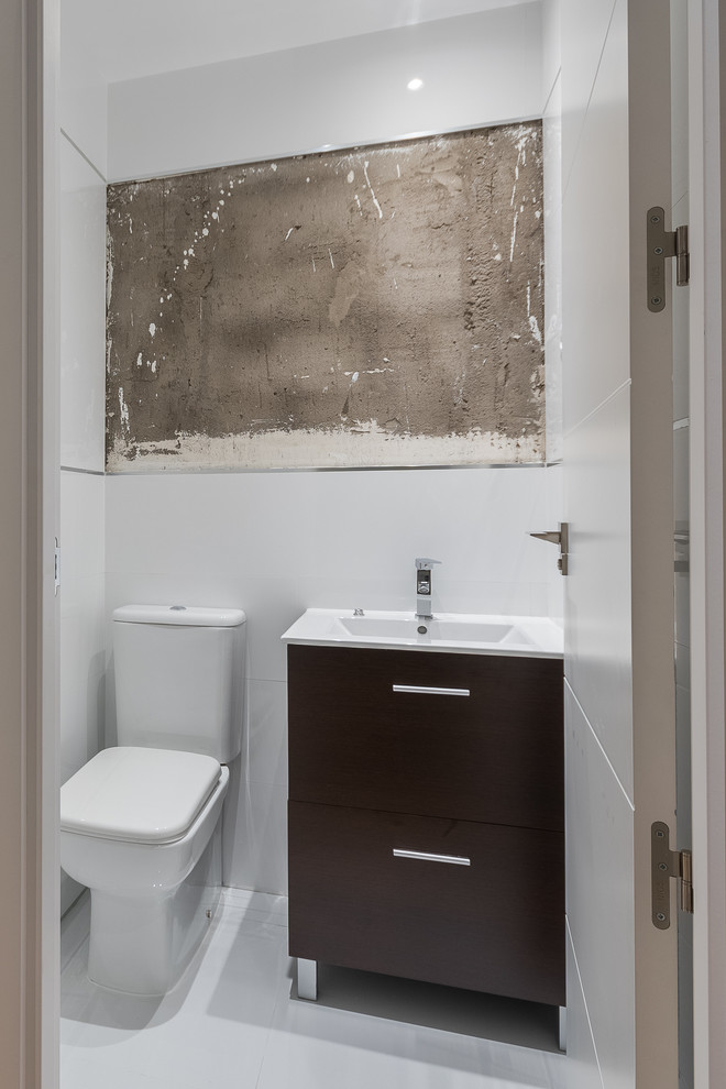 Kleine Moderne Gästetoilette mit flächenbündigen Schrankfronten, Wandtoilette mit Spülkasten, weißer Wandfarbe, integriertem Waschbecken und dunklen Holzschränken in Madrid