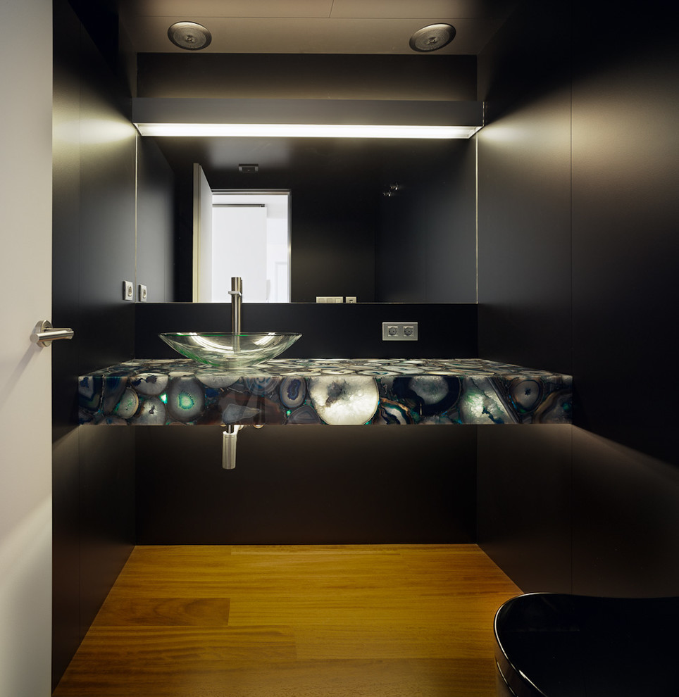 Imagen de aseo contemporáneo de tamaño medio con sanitario de pared, paredes negras, suelo de madera en tonos medios y lavabo sobreencimera