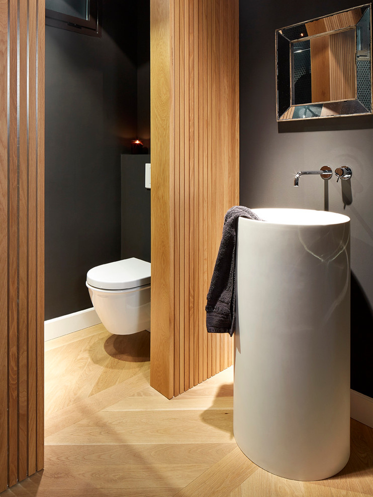 Inspiration för små moderna toaletter, med en vägghängd toalettstol, svarta väggar, ljust trägolv och ett piedestal handfat