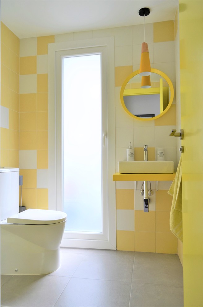 Modelo de aseo escandinavo con baldosas y/o azulejos amarillos, baldosas y/o azulejos de cerámica, paredes amarillas, suelo de baldosas de cerámica, lavabo sobreencimera, encimera de madera, suelo gris y encimeras amarillas