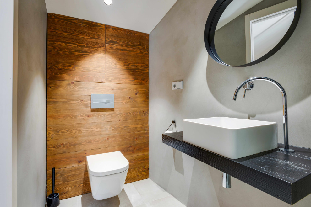 Moderne Gästetoilette mit Aufsatzwaschbecken, Waschtisch aus Holz, grauem Boden, schwarzer Waschtischplatte und Holzwänden in Sonstige