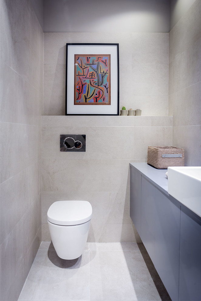 Exempel på ett litet modernt toalett, med grå skåp, en vägghängd toalettstol, grå kakel, grå väggar, släta luckor, keramikplattor och ett fristående handfat