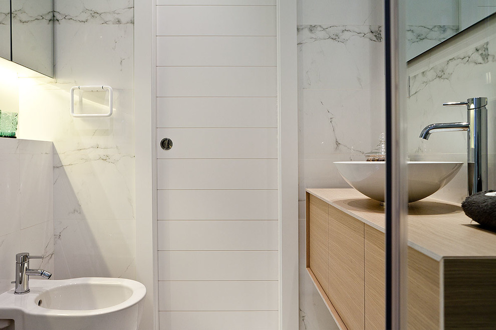 Источник вдохновения для домашнего уюта: туалет среднего размера в стиле неоклассика (современная классика) с плоскими фасадами, биде, белыми стенами, настольной раковиной и светлыми деревянными фасадами