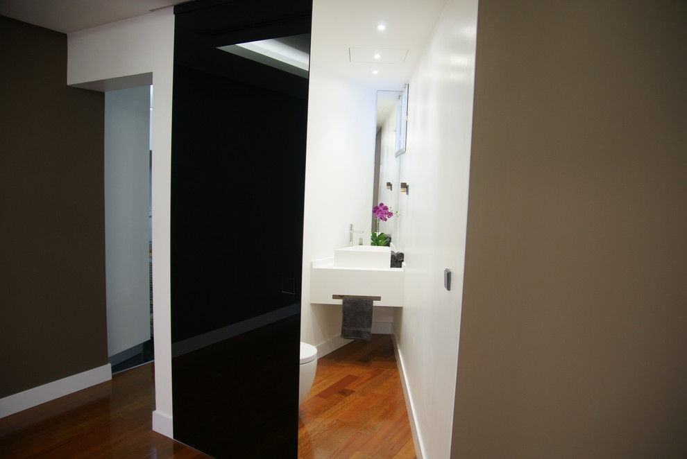 Réalisation d'un petit WC et toilettes minimaliste avec un urinoir, un mur blanc, un sol en bois brun et une vasque.