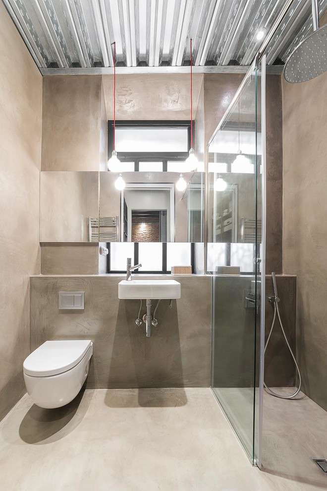 Große Industrial Gästetoilette mit Wandtoilette, grauer Wandfarbe, Betonboden und Wandwaschbecken in Barcelona