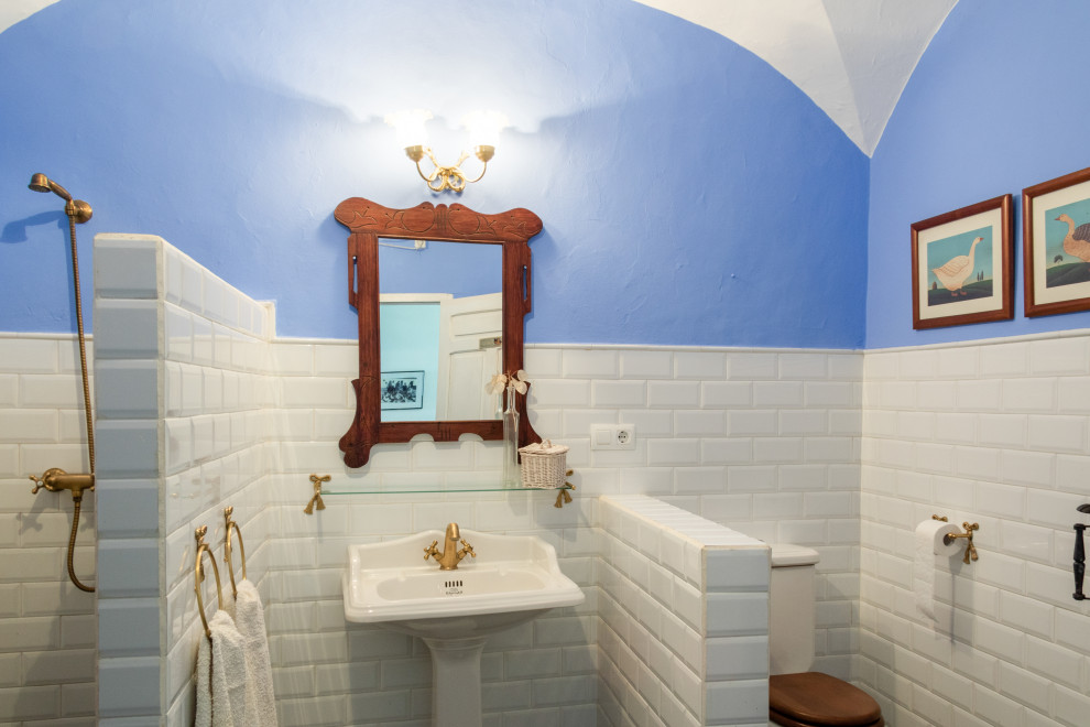 Photo of a small rustic cloakroom in Other with white cabinets, an urinal, white tiles, ceramic tiles, blue walls, slate flooring, a pedestal sink, black floors, a freestanding vanity unit, a vaulted ceiling and brick walls.