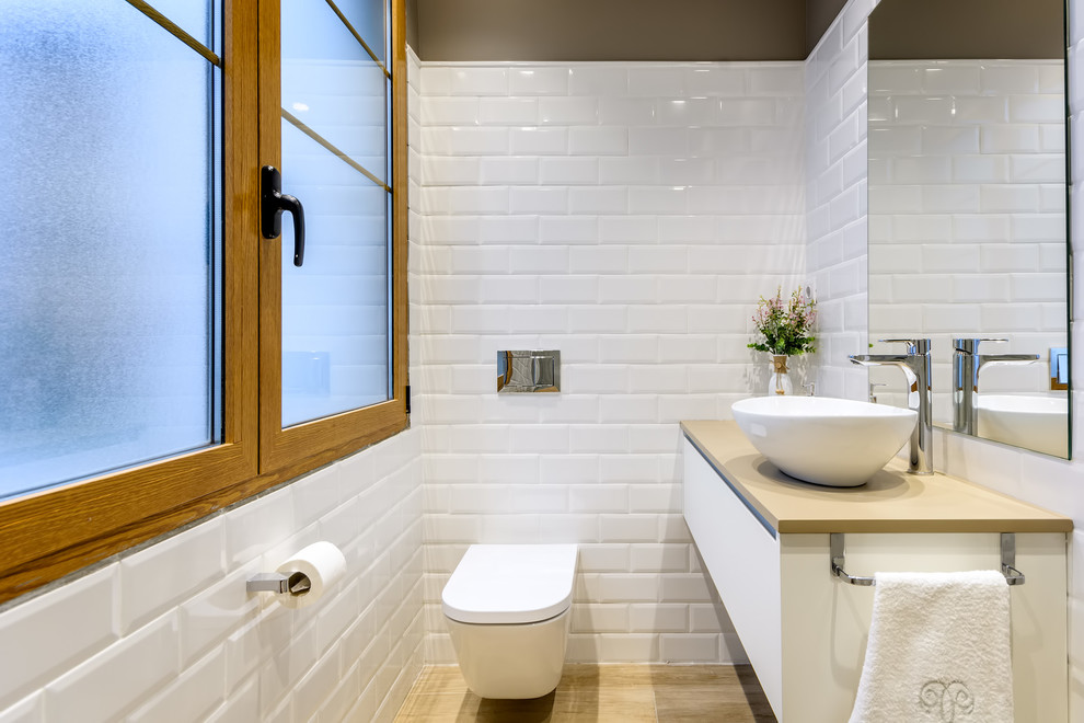 Exemple d'un petit WC suspendu tendance avec un placard à porte plane, des portes de placard blanches, un carrelage blanc, un carrelage métro, un mur marron, un sol en carrelage de porcelaine, une vasque, un sol marron et un plan de toilette beige.