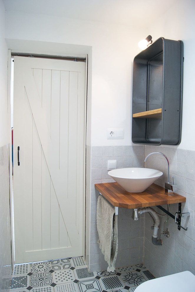 他の地域にある地中海スタイルのおしゃれなトイレ・洗面所 (黒いタイル、セラミックタイル、ベッセル式洗面器、木製洗面台) の写真
