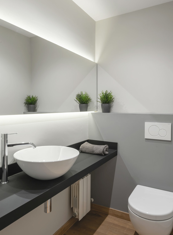 Esempio di un bagno di servizio minimalista con WC sospeso, pavimento in legno massello medio, top nero e pavimento marrone