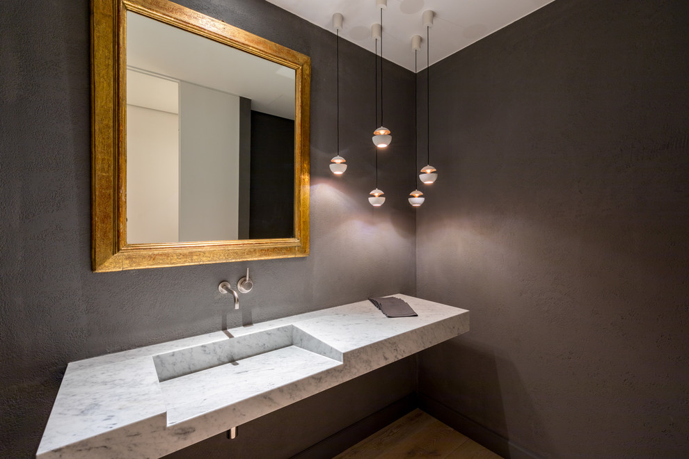 Diseño de aseo contemporáneo con paredes negras, suelo de madera en tonos medios, lavabo integrado, encimera de mármol, suelo beige y encimeras grises