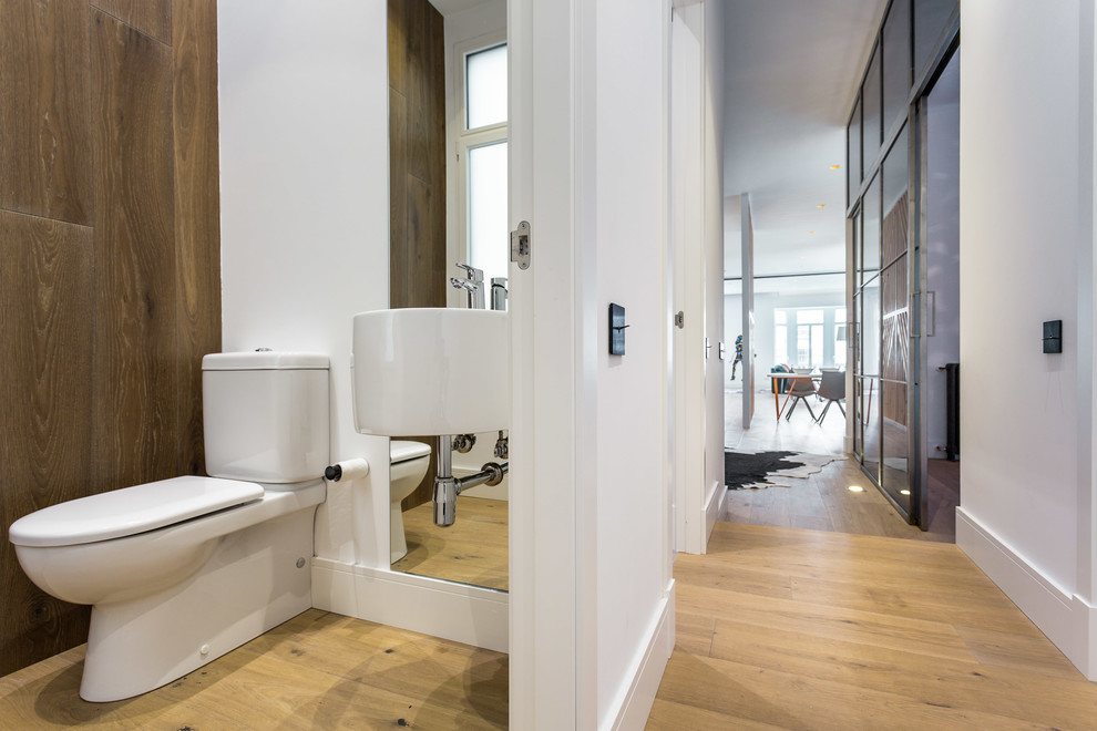 Immagine di un piccolo bagno di servizio design con WC a due pezzi, pareti bianche, pavimento in legno massello medio e lavabo sospeso