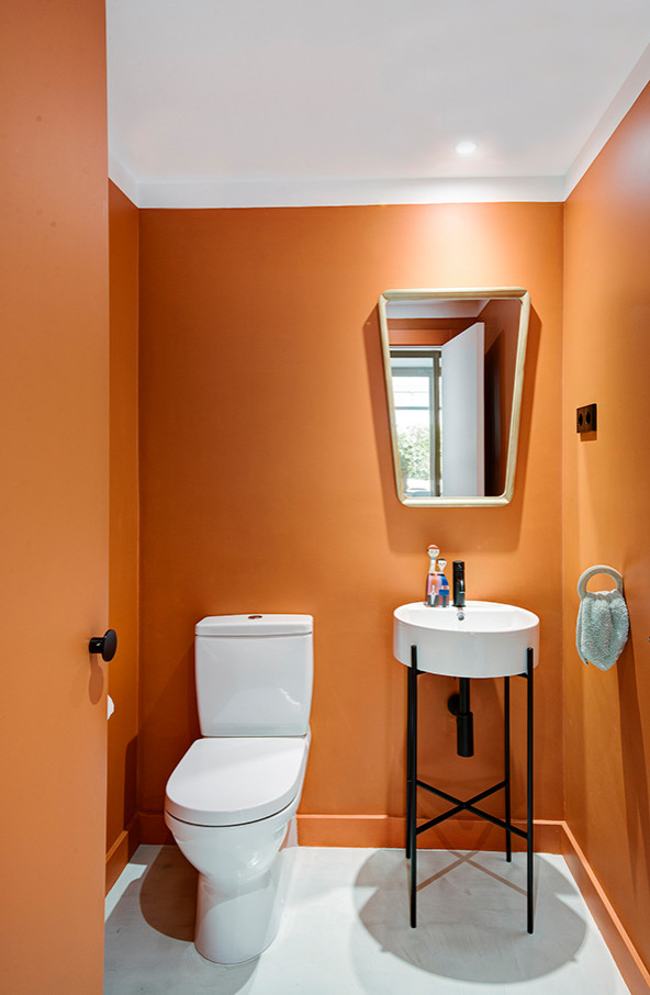 Modern cloakroom in Madrid with a wall mounted toilet, orange tiles, orange walls, concrete flooring, a vessel sink and grey floors.