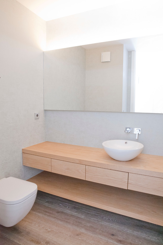 Esempio di un piccolo bagno di servizio minimalista con ante lisce, ante in legno chiaro, WC sospeso, pareti bianche, lavabo a bacinella e parquet chiaro