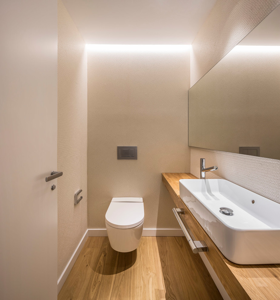 Idée de décoration pour un petit WC et toilettes design avec WC à poser, un carrelage beige, un mur beige, un sol en bois brun, une vasque, un plan de toilette en bois, un sol marron et un plan de toilette marron.