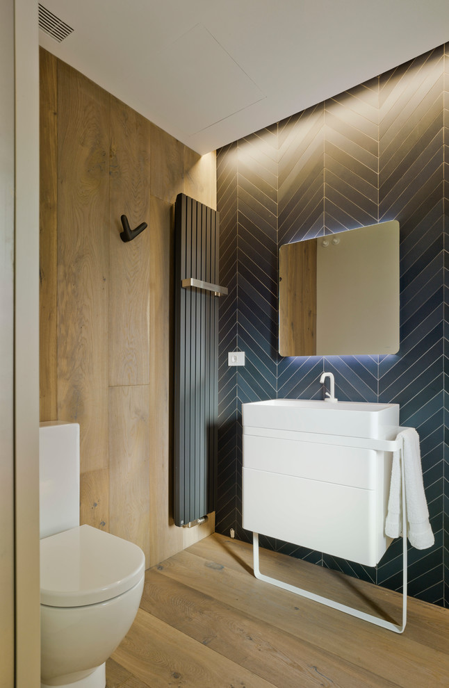 Small trendy black tile medium tone wood floor and brown floor powder room photo in Alicante-Costa Blanca with a two-piece toilet, black walls, flat-panel cabinets, white cabinets and a console sink