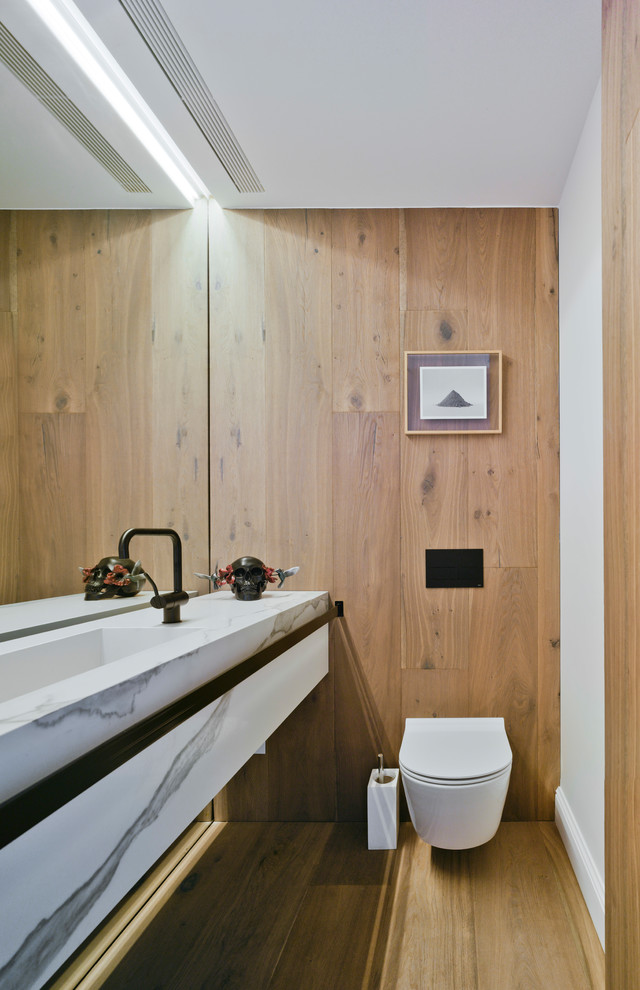 Cette photo montre un petit WC suspendu tendance avec un mur blanc, un sol en bois brun, un lavabo intégré, un plan de toilette en marbre et un sol marron.