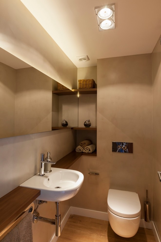 Modelo de aseo contemporáneo de tamaño medio con sanitario de pared, paredes beige, suelo de madera en tonos medios, lavabo suspendido y encimera de madera